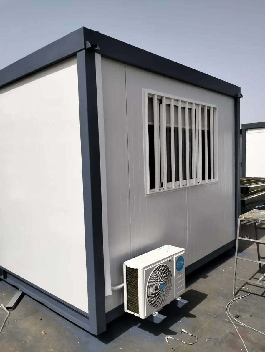 Petit module monobloc en panneaux sandwich blancs, fenêtre à barreaux et climatiseur, adapté à un poste de garde