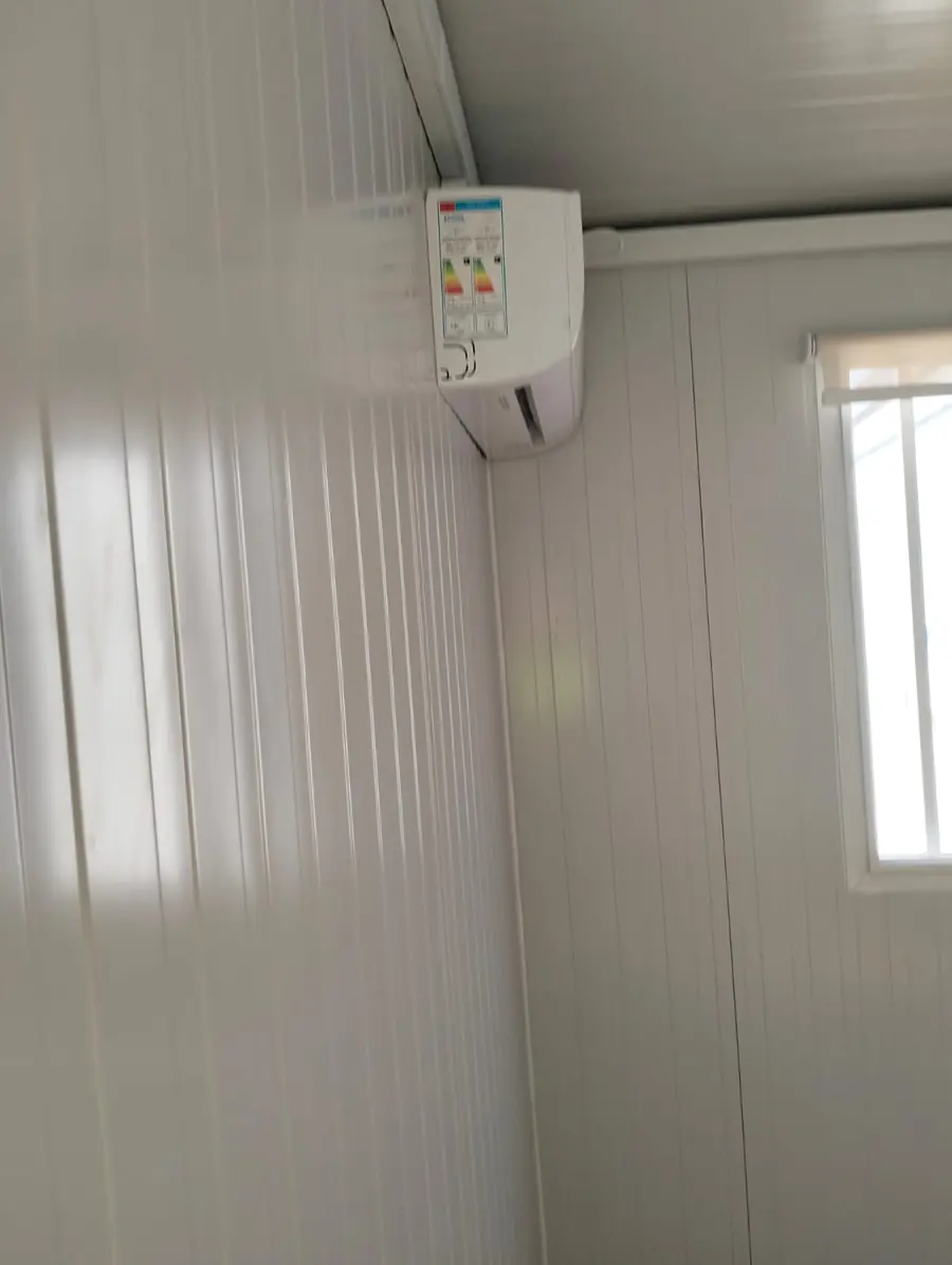 Unité intérieure de climatiseur split fixée en haut d'un mur en panneaux blancs, près d'une fenêtre, dans un bureau modulaire