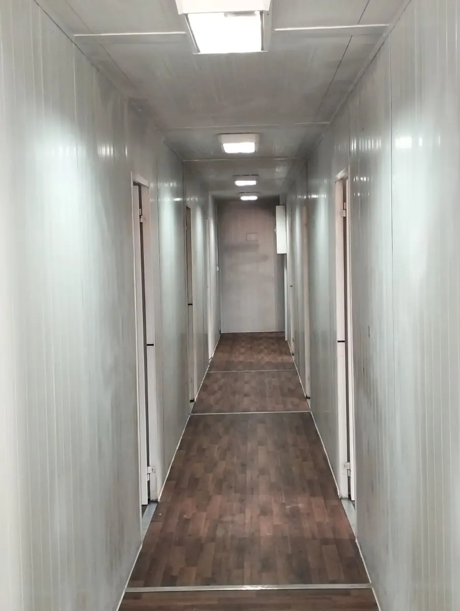 Couloir central d'un dortoir modulaire avec portes de chambres de part et d'autre, sol imitation parquet et plafonniers