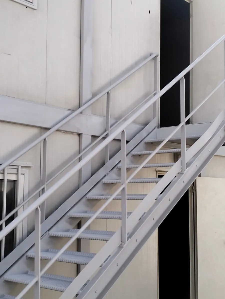 Escalier métallique boulonné à marches en caillebotis et double main courante desservant l'étage de modules superposés