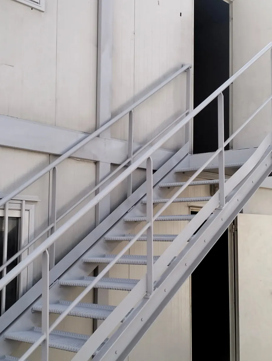 Escalier métallique boulonné à marches en caillebotis et garde-corps tubulaires, desservant l'étage de modules préfabriqués