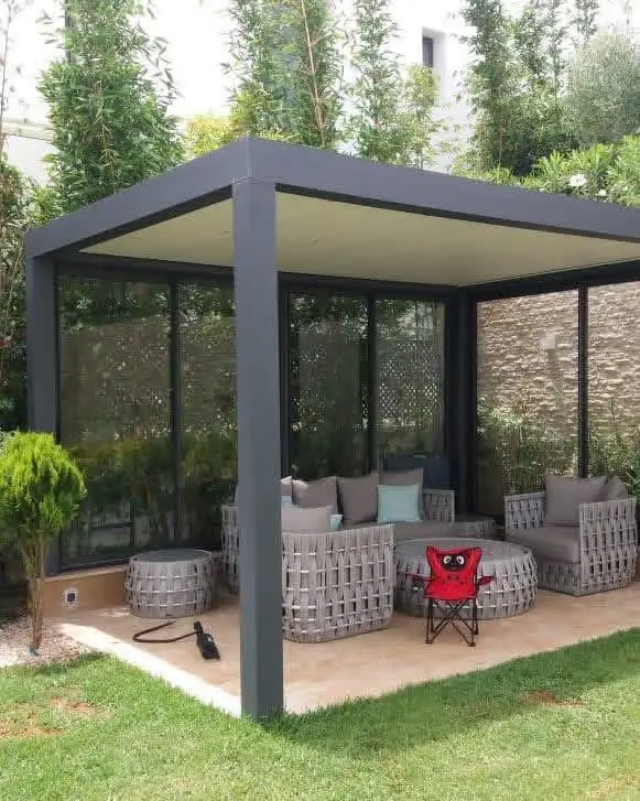 Pergola métallique gris anthracite à toit plein au-dessus d'un salon de jardin, avec panneaux vitrés sur les côtés