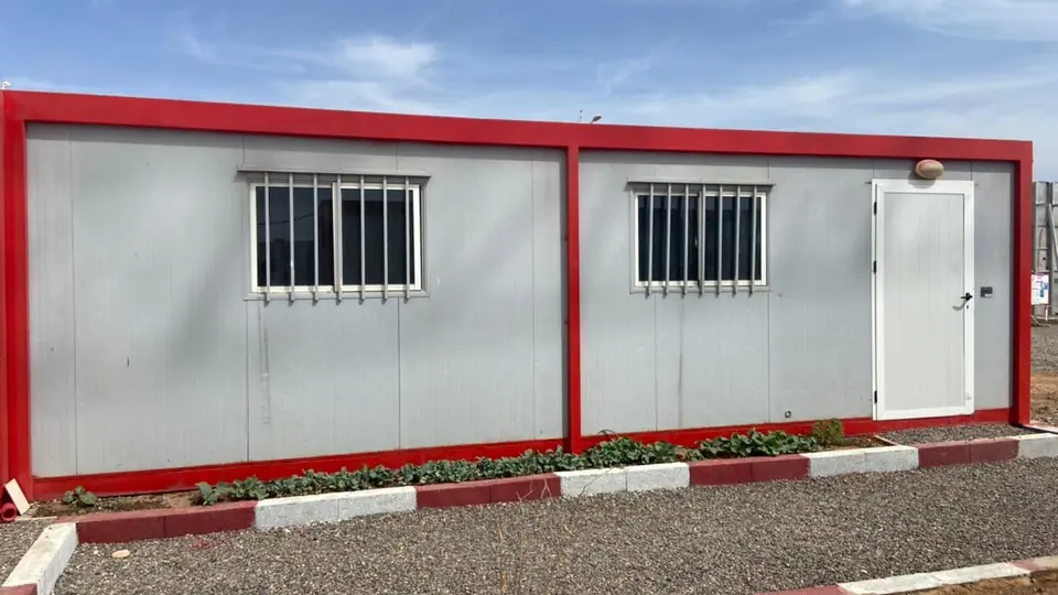 Bâtiment modulaire à cadre rouge et panneaux gris, fenêtres à barreaux, chantier de remise en état à Marrakech