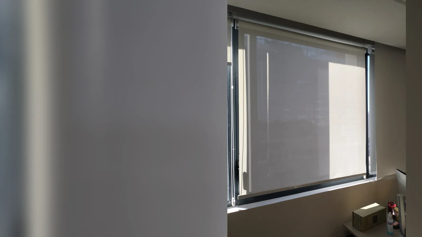 Store enrouleur screen beige baissé devant la fenêtre ensoleillée d'un bureau, vue extérieure visible