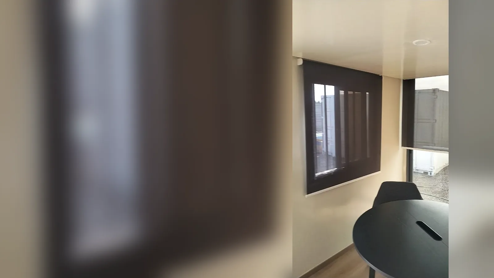 Store enrouleur screen sombre baissé devant la fenêtre d'une salle de réunion en bâtiment modulaire